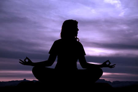 A silhouette of a woman doing a meditating pose in the outdoors.の写真素材