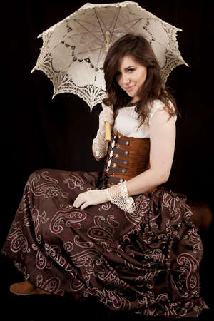 A woman with a small smile on her face holding on to her umbrella in a vintage western dressの写真素材