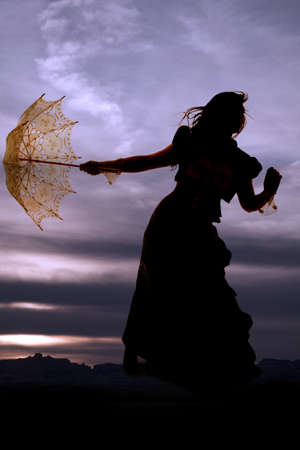 A silhouette of a woman holding on to her umbrella as the wind blows her hair.の写真素材