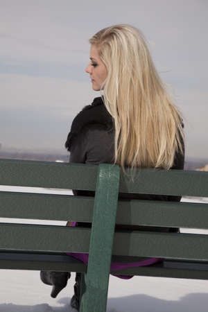A woman sitting on a green park bench in the winter at a park thinking.の写真素材