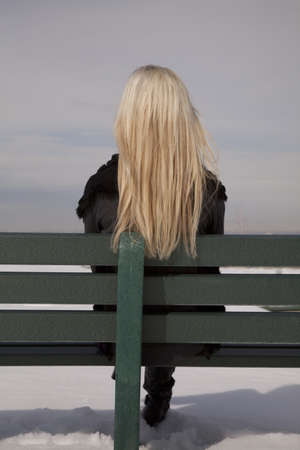 a woman sitting on her green bench with snow on the ground.with her back to the camera.の写真素材