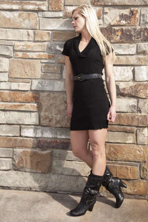 A woman standing up against a brick wall looking down with a sad expression on her face.の写真素材