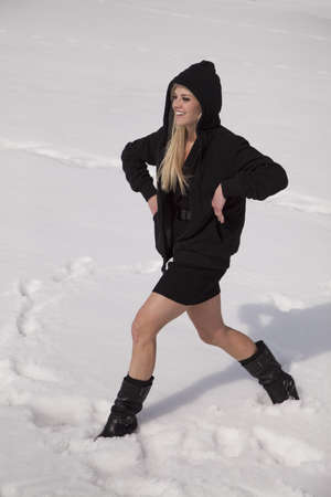A woman in her black skirt smiling and laughing while walking through snow.の写真素材