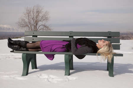 A woman laying back on a park bench in her dress resting.の写真素材