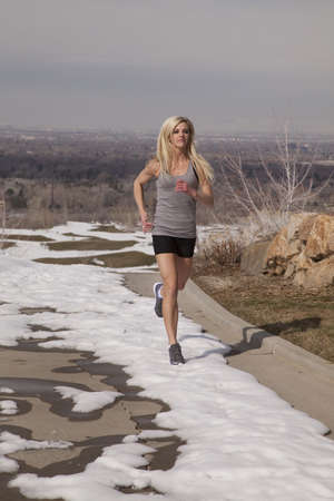 A woman running in the snow trying to be healthy and fit.の写真素材