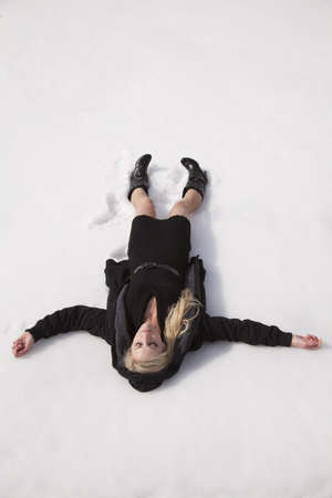A woman laying in the snow in her black dress.の写真素材