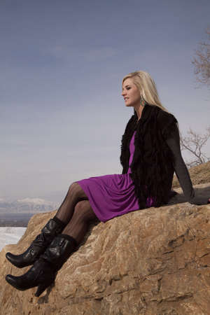 A woman sitting on a rock in her dress in the outdoors with a smile on her face.の写真素材