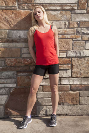 A woman in her fitness clothes standing by a brick wall.の写真素材