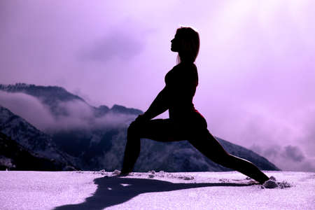 A silhouette of a woman stretching out her body in the snow in the outdoors.の写真素材