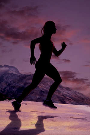 a silhouette of a woman running through the snow.の写真素材