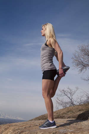 A woman lifting up her leg to stretch in the outdoors.の写真素材