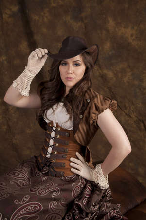 A woman with a serious expression sitting in her vintage western dress and hat.の写真素材