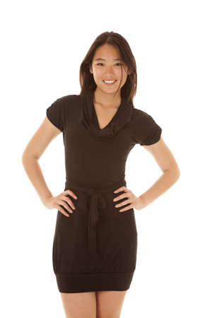 A woman with a smile on her face in her black dress and her hands on her hipsの写真素材