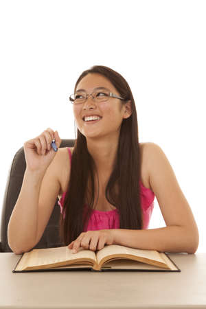 A woman looking up and laughing while she is holding a pen and pointing at a bookの写真素材