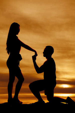 A silhouette of a man kneeling down and proposing to his girlfriend.の写真素材