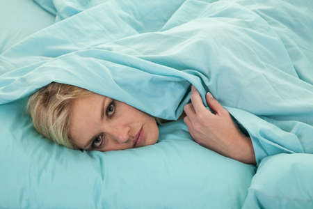 a woman with her head covered by her sheet peeking out from underneath her sheet.の写真素材