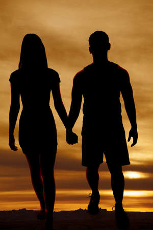 a silhouette of a man and woman holding hands walking.の写真素材