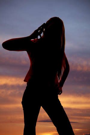 Woman talking on a cell phone silhouette in front of a sunset.の写真素材