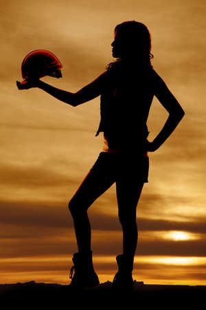 a silhouette of a woman holding on to her hard hat with a beautiful sky behind her.の写真素材