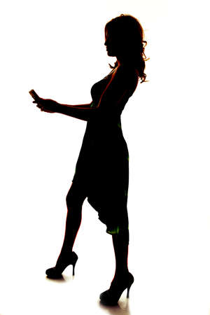 a silhouette of a woman holding on to her cell phone sending a textの写真素材