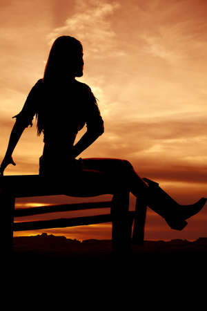 a silhouette of a woman sitting on a bench with a beautiful skyの写真素材