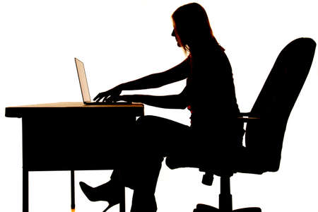 Silhouette of a woman sitting at a desk typing on a computer.の写真素材
