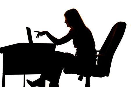 Silhouette of a woman sitting at a desk pointing at computer.の写真素材