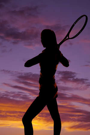 A silhouette of a woman holding on to her racquet with a beautiful sky behind her.の写真素材