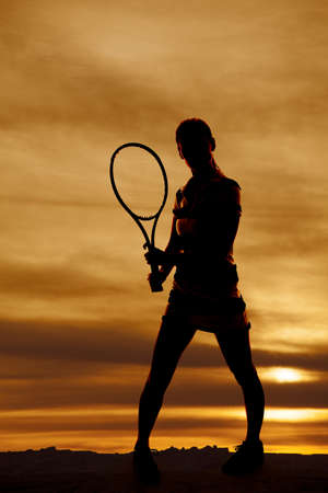 A woman holding on to a tennis racket with a beautiful sky behind her.の写真素材