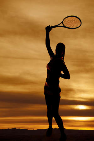 A silhouette of a woman swinging her racquet with a colorful sky behind her.の写真素材