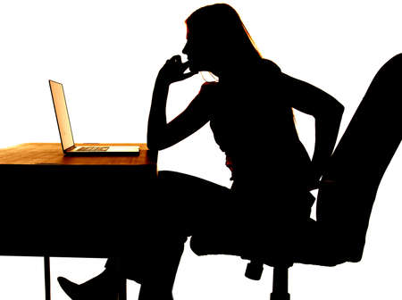 Silhouette of a woman sitting at a desk with a computer thinking.の写真素材