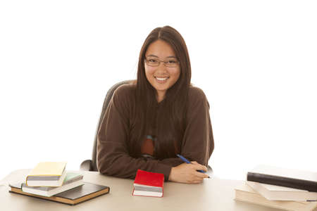 a student sitting at her desk with books and a pen smiling.の写真素材