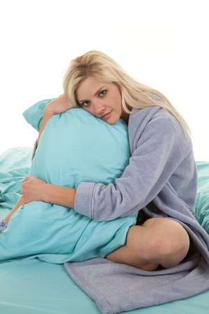 A woman sitting in her bed in her robe snuggling her pillow.の写真素材