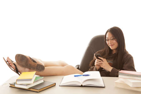 a student with her feet up on the desk using her phone to text instead of doing her workの写真素材