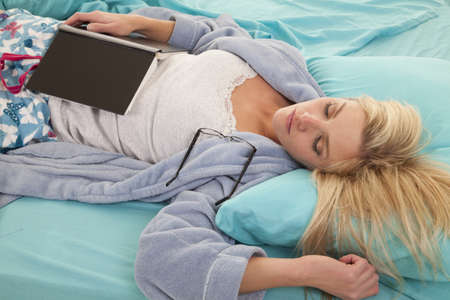 a woman laying in bed with her book and her glasses have fallen off.の写真素材