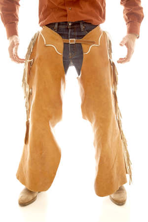 A cowboy in chaps standing with his hands ready.