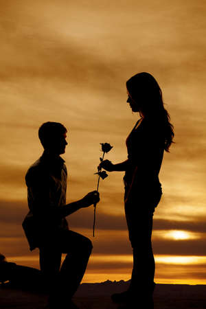 A man is on one knee handing a woman a rose in the sunset.の写真素材