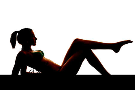 A silhouette of a sexy woman sitting back on her elbows with one foot up.の写真素材