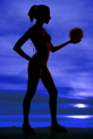 A woman is silhouetted in the sky holding a volleyballの写真素材