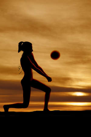 A woman is passing a volleyball in the sunset.の写真素材