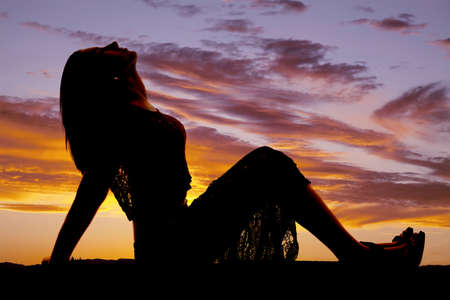 A woman in a lace skirt is sitting silhouetted leaning back.の写真素材