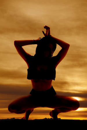 A woman in the sunset silhouette squat.の写真素材