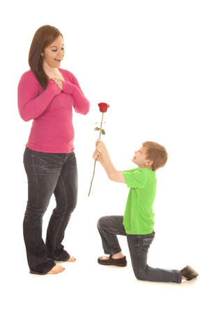 A young boy is on his knee giving a rose to a woman.の写真素材