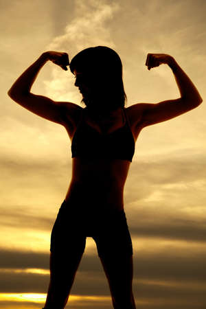 A silhouette of a woman flexing her arms with a beautiful sky behind her.の写真素材