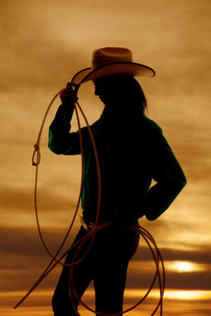 A silhouette of a woman with a rope and cowgirl hat, with a beautiful sunset in the background.の写真素材