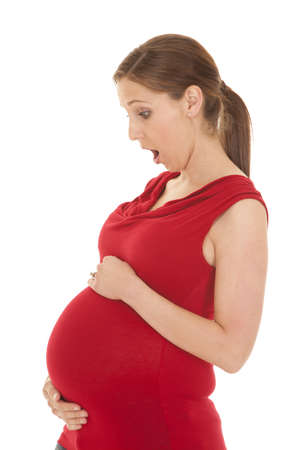 A pregnant woman in a red shirt looking down at her belly in shock.の写真素材