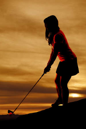 A silhouette of a woman golfing, with a beautiful sky behind her.の写真素材