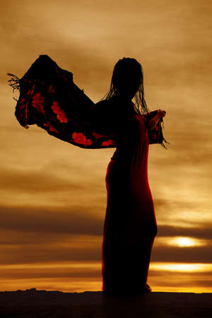 a silhouette of a woman in her dress with her sarong blowing in the wind.の写真素材