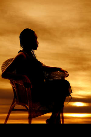 A silhouette of a woman sitting in a wicker chair.の写真素材