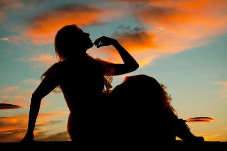 A silhouette of a woman with her hand on her chin in her dress sitting.の写真素材